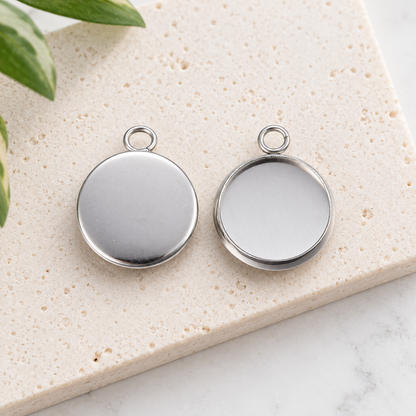 Front and back view of 12mm round stainless steel pendant settings on a light stone background, showing the bezel cup and smooth reverse side.