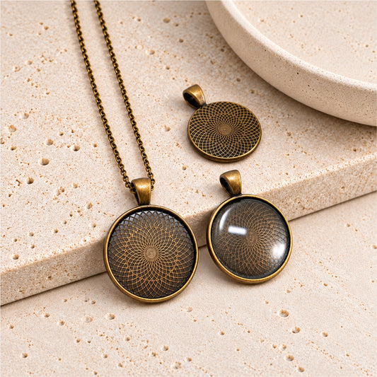 Antique bronze round pendant settings with geometric patterns for 25mm glass cabochons, displayed on beige stone.