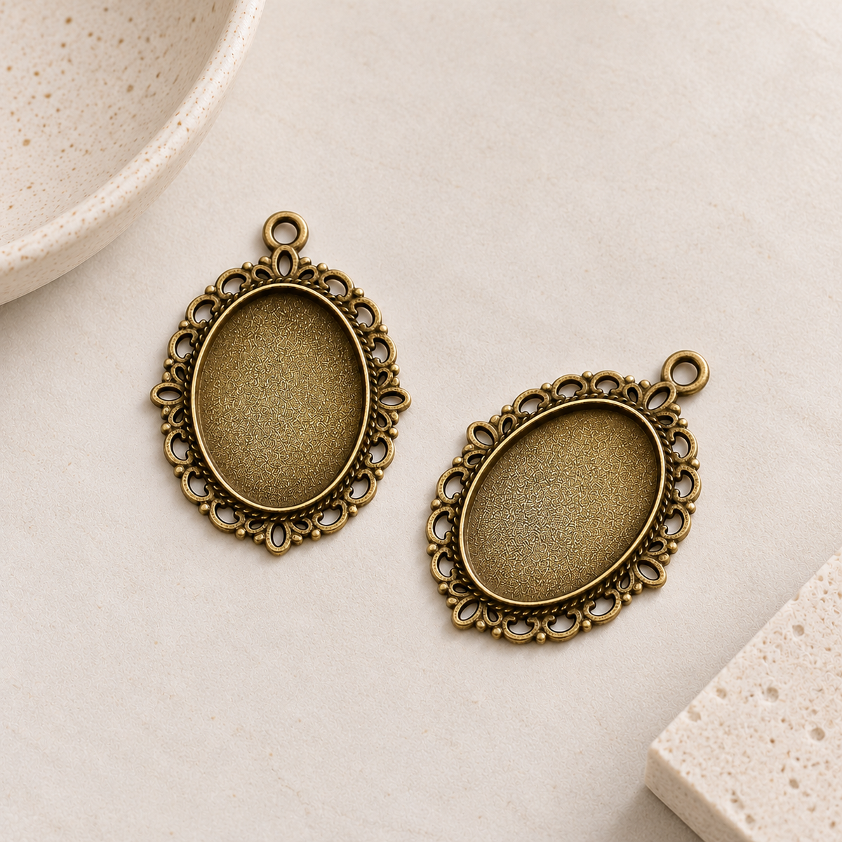 Two antique bronze oval pendant settings with decorative filigree borders, designed for 18x25mm cabochons.