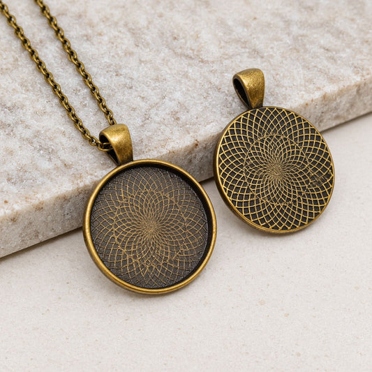 Two antique bronze round pendant settings with decorative patterned bases, displayed on a neutral stone background for DIY jewelry making.