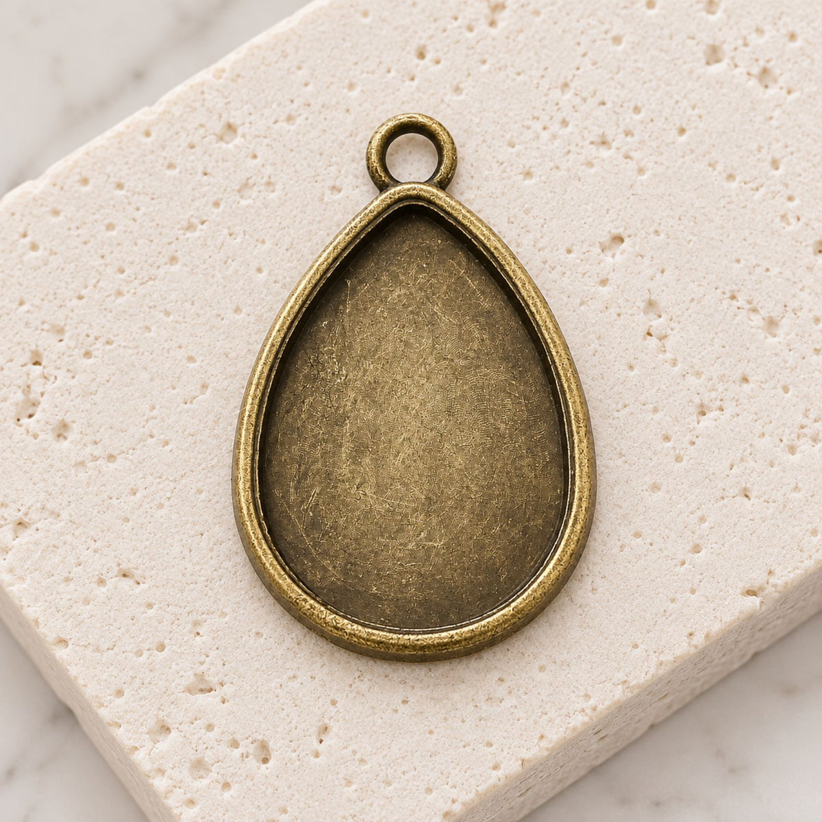 Two antique bronze teardrop pendant trays displayed on a neutral background for jewelry making.