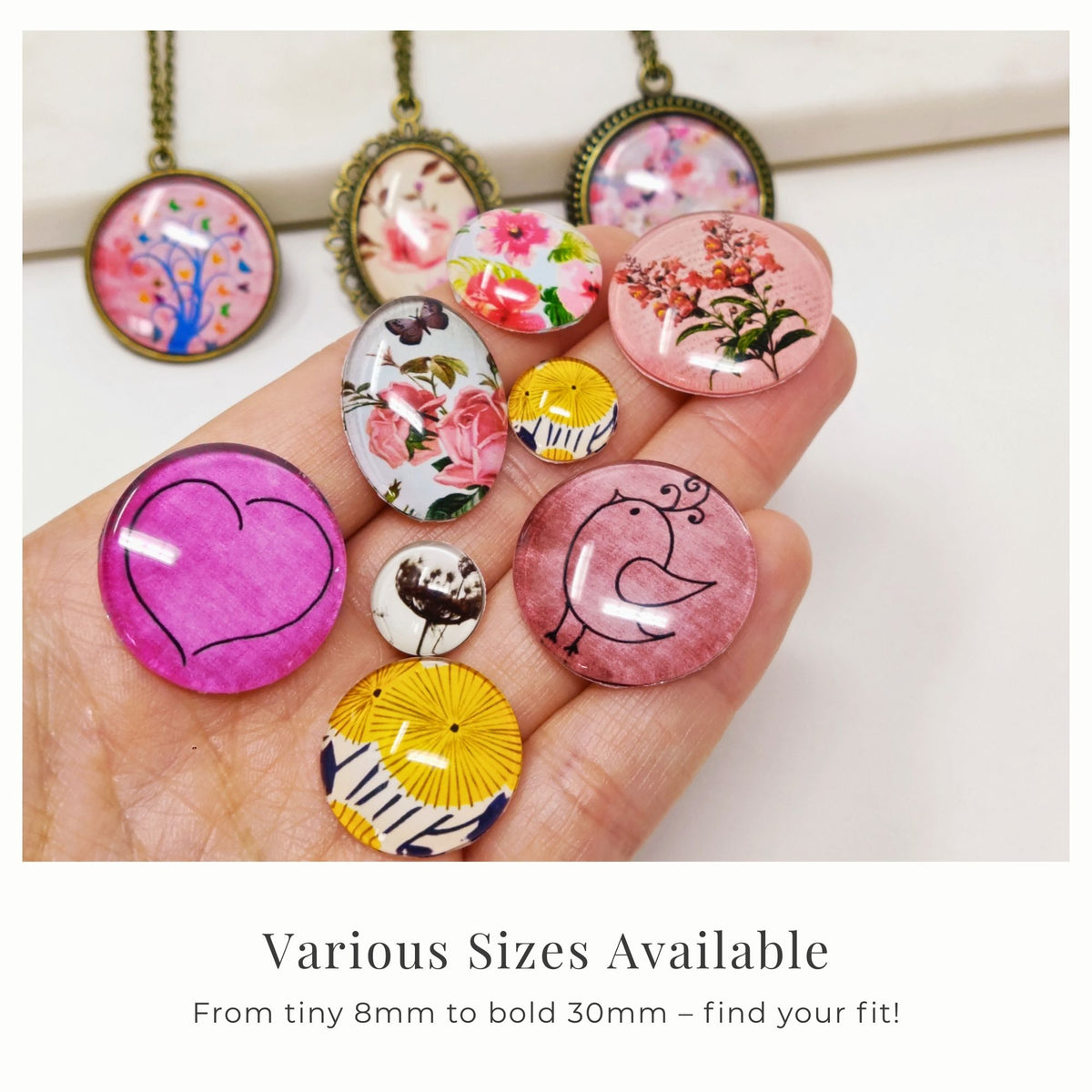 Round glass dome cabochons in assorted sizes and designs displayed on a hand for size comparison