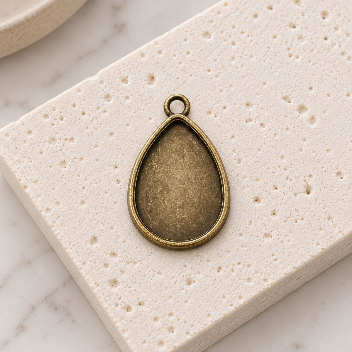 Close-up of vintage-style bronze teardrop pendant settings with recessed bases for handmade cabochon necklaces.