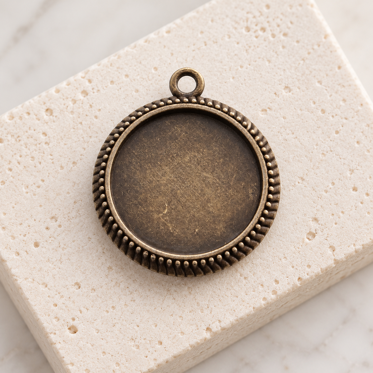 Vintage bronze round pendant blanks with 25mm cabochon trays displayed on a neutral stone background.