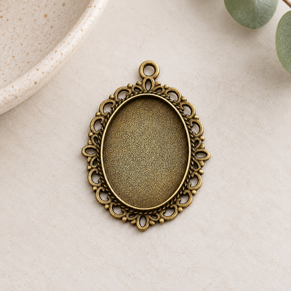 Vintage-style bronze oval pendant blanks with ornate edges, displayed on a soft neutral background for handmade jewelry projects.