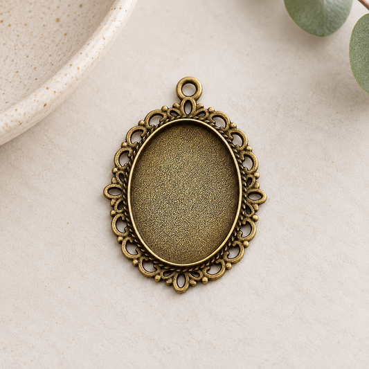 Vintage-style bronze oval pendant blanks with ornate edges, displayed on a soft neutral background for handmade jewelry projects.