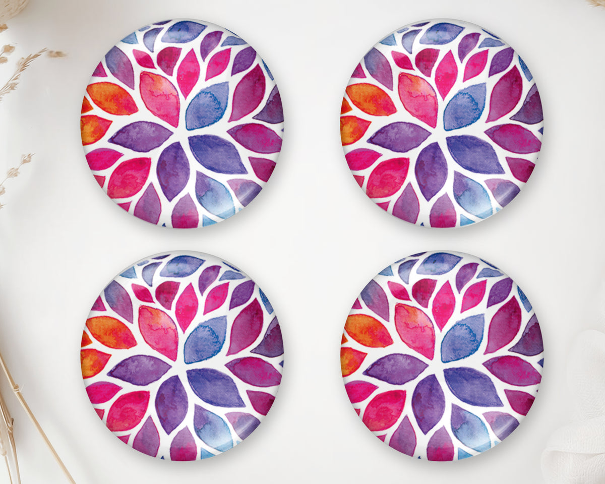 Four round glass cabochons with colorful watercolor leaves in pink, purple, orange and blue on a white background