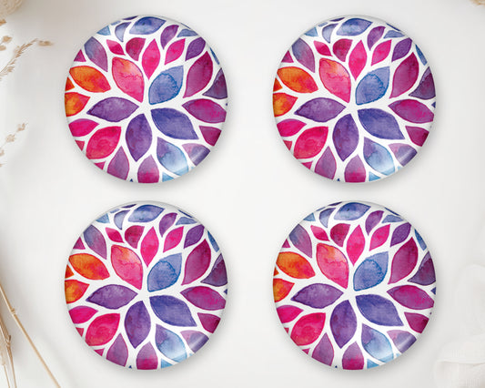 Four round glass cabochons with colorful watercolor leaves in pink, purple, orange and blue on a white background